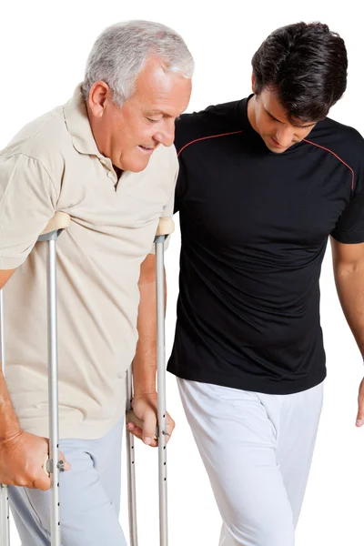 Trainer helpen van senior man met krukken — Stockfoto