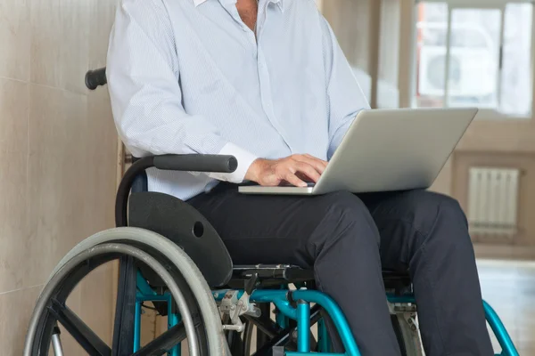 Hombre sentado en silla de ruedas usando el ordenador portátil —  Fotos de Stock