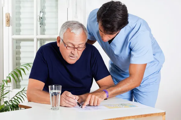 Enfermera masculina ayudando a un hombre mayor en la resolución de rompecabezas — Foto de Stock