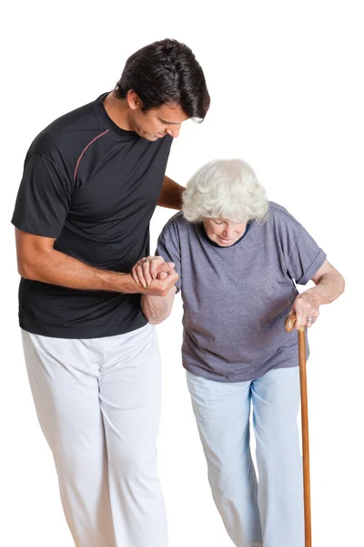 Entrenador asistiendo a la mujer mayor sosteniendo el bastón —  Fotos de Stock