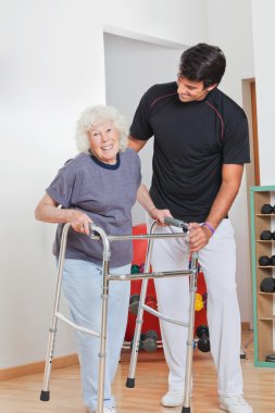 Senior Woman Holding Walker While Trainer Assisting Her clipart