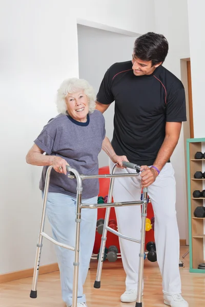 Anziana donna holding walker mentre trainer assistere il suo — Foto Stock