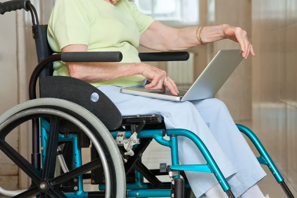 Femme âgée assise en fauteuil roulant en utilisant un ordinateur portable — Photo