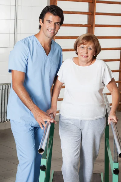 Terapeuta que ayuda a la mujer mayor a caminar con el apoyo de la barra — Foto de Stock