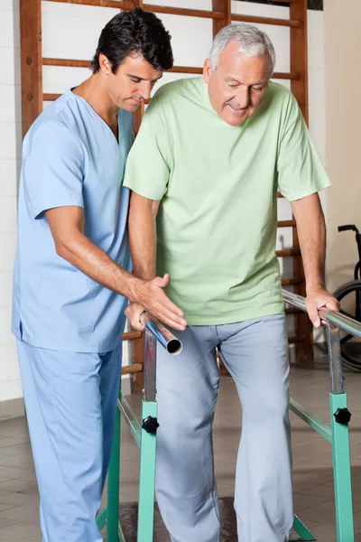 Terapeuta que ayuda al hombre mayor a caminar con el apoyo de las barras — Foto de Stock
