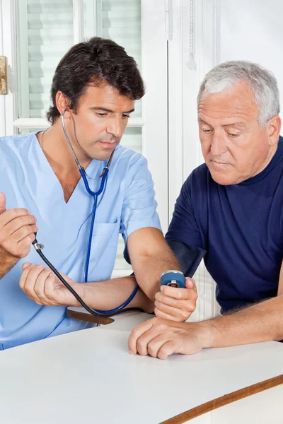 Enfermeira masculina verificando a pressão arterial de um homem sênior — Fotografia de Stock