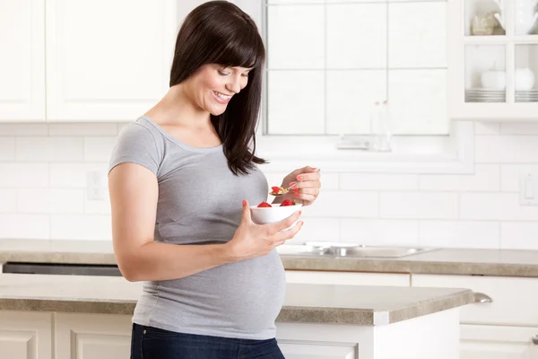 Беременная женщина на кухне ест закуски — стоковое фото