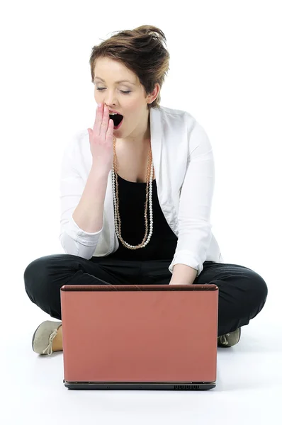 Молодая женщина сидит на полу зевая, скучно с ноутбуком изолированы — стоковое фото