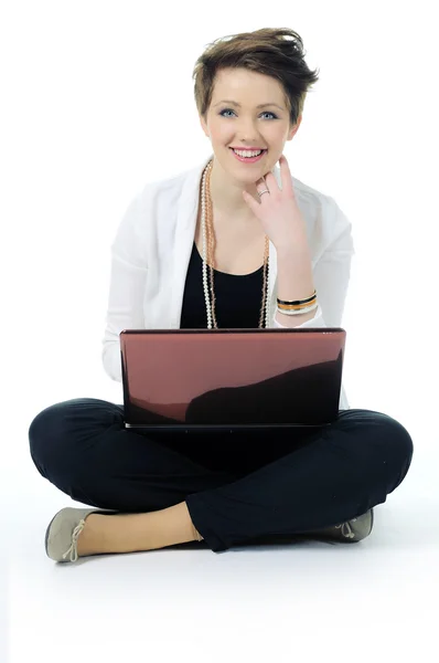 Mujer joven sonriendo sentado en el suelo con el ordenador portátil aislado en blanco —  Fotos de Stock