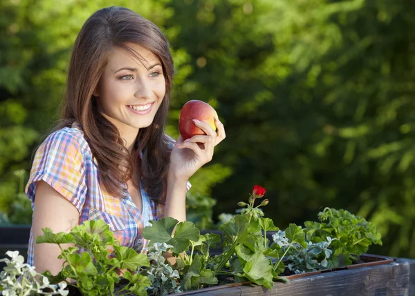 Portret van meisje met rode appel tegen groene tuin. — Stockfoto