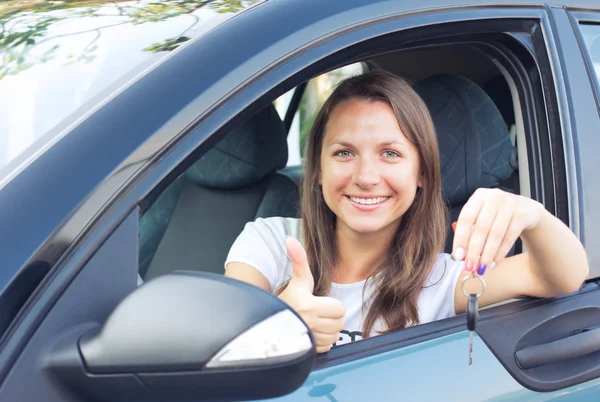 Mladá dívka sedící v autě a ukazuje klíč — Stock fotografie