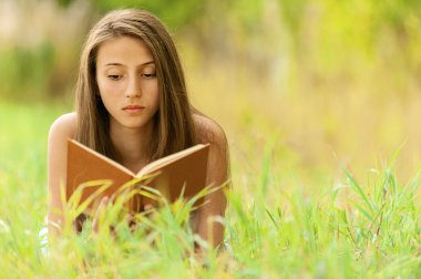 Woman lying on grass reading book clipart