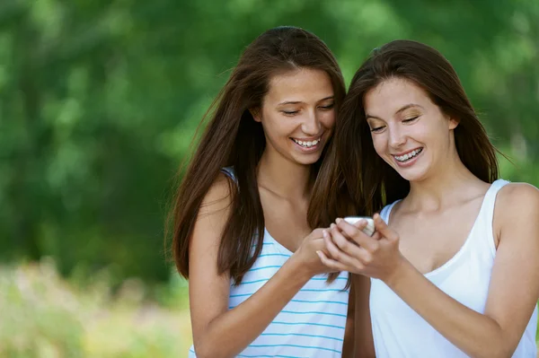 Dos chicas encantadoras lee el mensaje al teléfono móvil —  Fotos de Stock