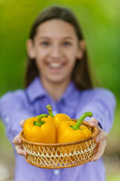 Teenage girl shows basket with orange peppers — Stock Photo, Image
