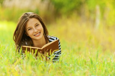 Smiling woman lying on grass reading book clipart