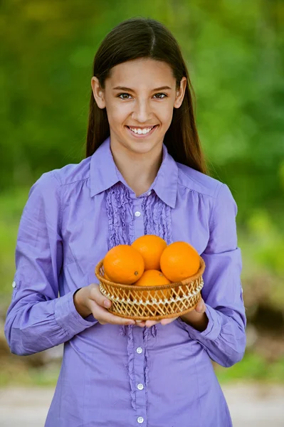 Улыбающаяся девочка-подросток держит корзину апельсинов — стоковое фото