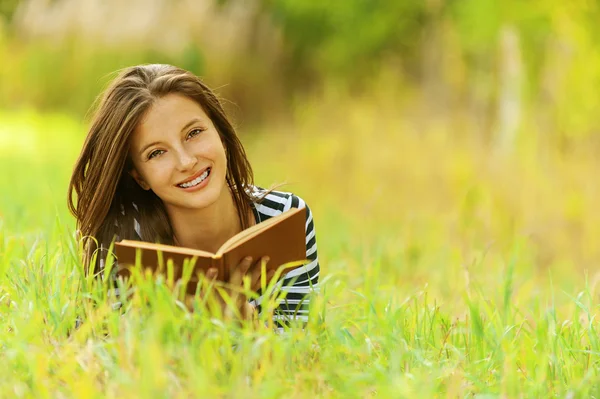 Sorrindo mulher deitada no livro de leitura grama — Fotografia de Stock