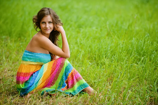 Mulher em vestido colorido sentado na grama — Fotografia de Stock