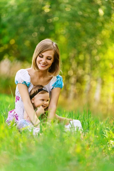 Kobieta i jej córeczka, siedząc na trawie — Zdjęcie stockowe
