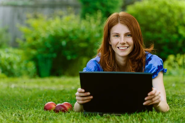 Jonge vrouw liggen op gras met laptop — Stockfoto