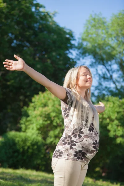 Женщина с открытыми руками наслаждается солнцем в парке — стоковое фото