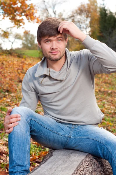 Outdoors portrait of happy young man sitting in autumn park — Stock Photo, Image