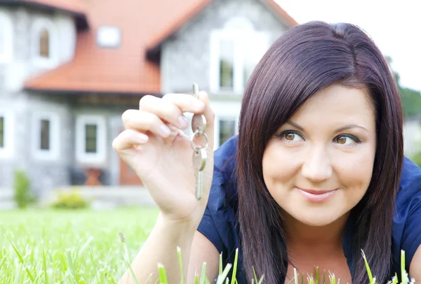 Woman holding keys with house background — Stock Photo, Image