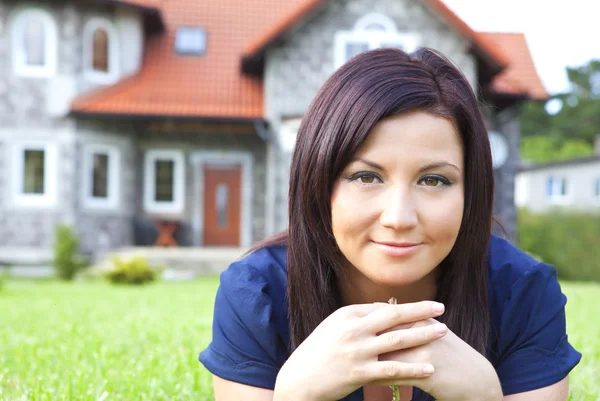 Женщина держит ключи с домом на заднем плане — стоковое фото