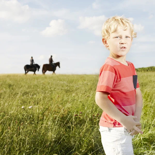 Young blonde boy standing in a grassy field — Stock Fotó