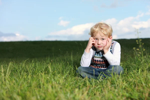 Smutný malý chlapec sedí v trávě — Stock fotografie