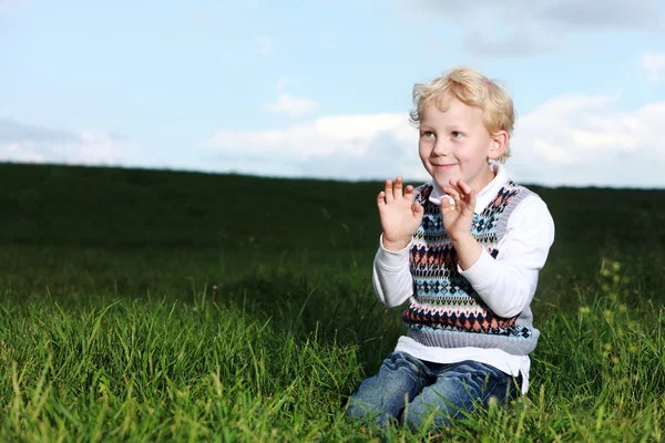 Ondeugende jongetje knielen in groene veld — Stockfoto