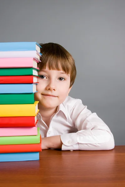 Boy looks out from a stack of books — Stock Photo, Image