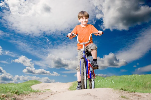 เด็กชายบนจักรยานบนพื้นหลังของท้องฟ้าสีฟ้า — ภาพถ่ายสต็อก