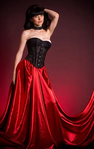 Sexy jonge vrouw in de mode jurk op rode achtergrond. — Stockfoto