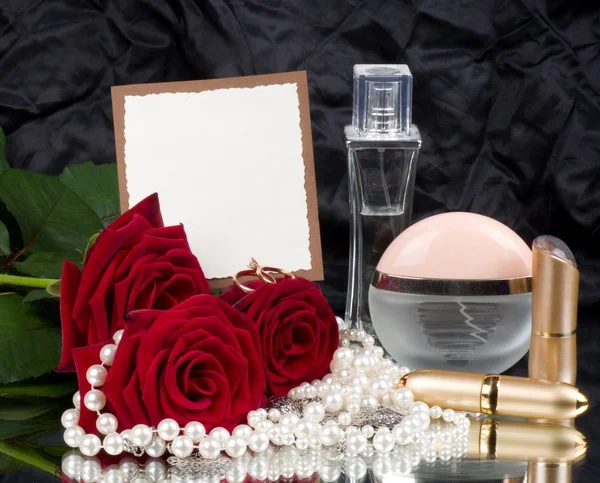 Beautiful perfume bottles, pink roses and beads with banner — Stock Photo, Image