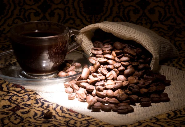 Xícara de café e saco de grãos de café contra fundo escuro — Fotografia de Stock