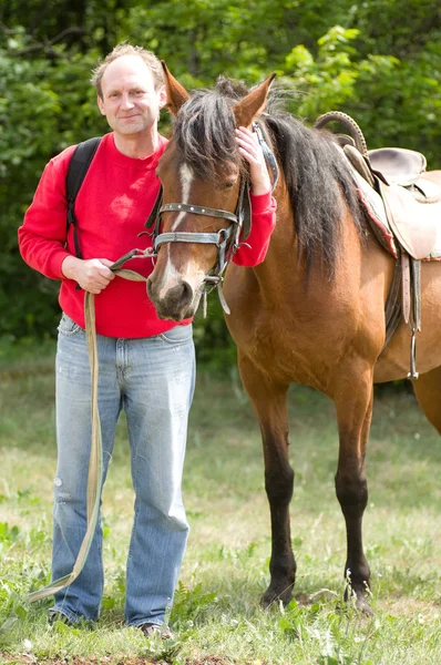 Guapo hombre sonriente con caballo en el bosque — Foto de Stock
