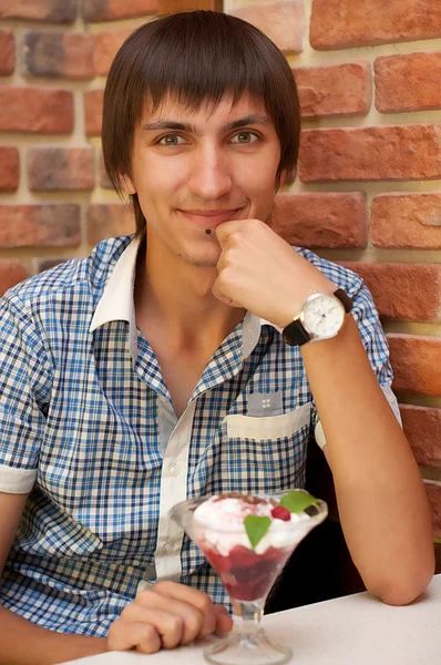 Young man sitting at cafe with cherry ice cream