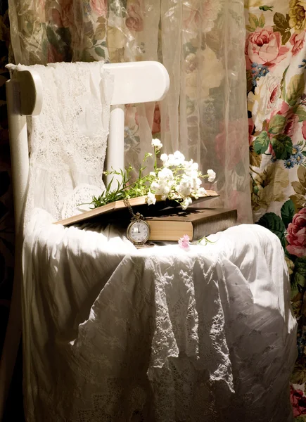 Fiori, libri, orologio e stoffa femminile sulla sedia bianca — Foto Stock