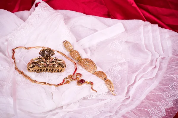 Zlaté šperky a bílé krajky na červeném pozadí — Stock fotografie