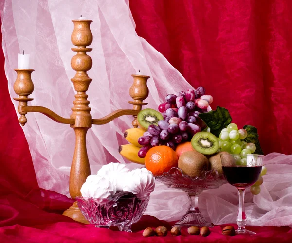 Bella composizione con frutta, candeliere e vino su vetro su sfondo rosso — Foto Stock