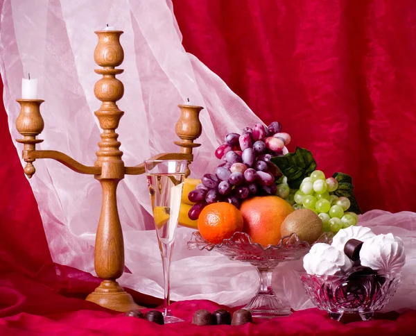 Beautiful composition with fruits, candlestick and wine on glass on red background — Stock Photo, Image