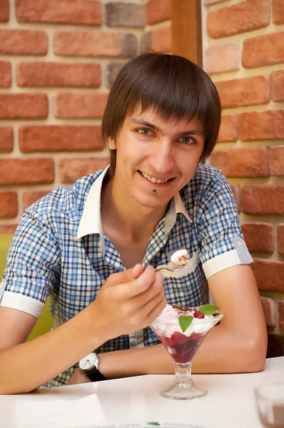 Mladý muž sedí v kavárně s třešňová zmrzlina — Stock fotografie