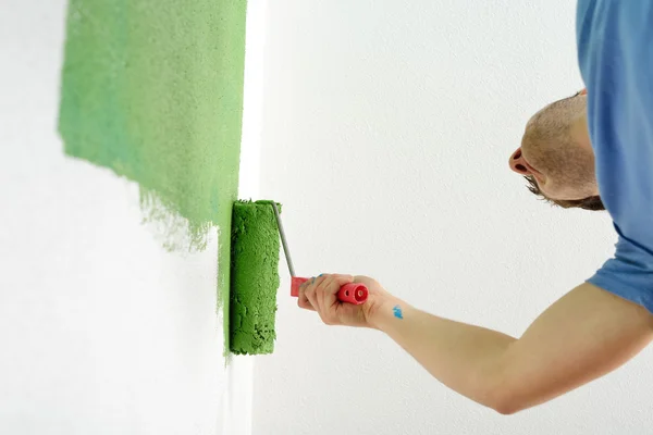 Pohledný mladý muž malujte bílou stěnu v barvě — Stock fotografie