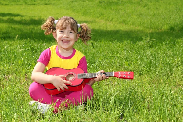 Pieni tyttö istuu nurmikolla ja soittaa kitaraa — kuvapankkivalokuva