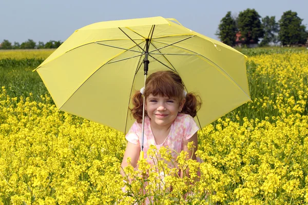 Schönes kleines Mädchen mit Regenschirm, das im gelben Blumenfeld steht — Stockfoto