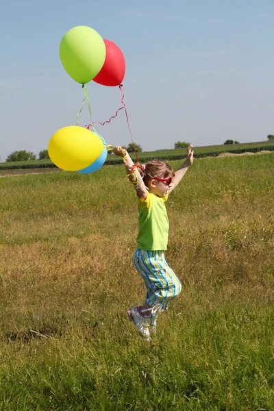 Kleines Mädchen rennt mit Luftballons auf Feld — Stockfoto