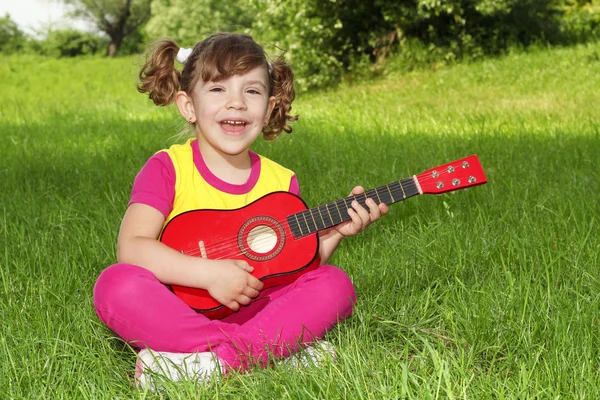 Küçük kız çimlere oturup gitar çalıp şarkı — Stok fotoğraf