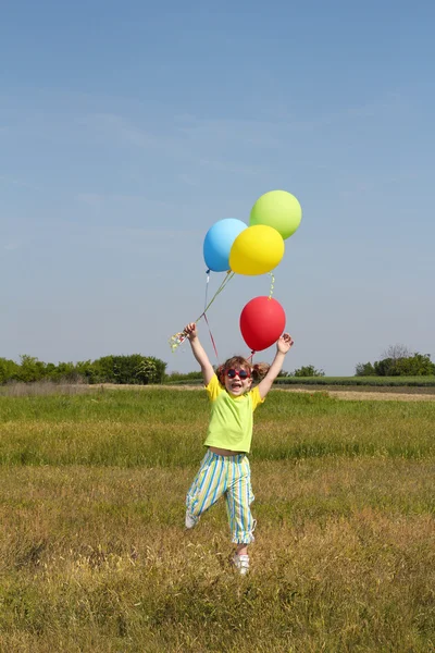 Happy little girl with balloons jumping on field — Stock Photo, Image
