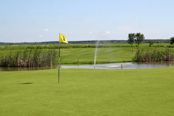 Гольф поле с желтым флагом и прудом — стоковое фото